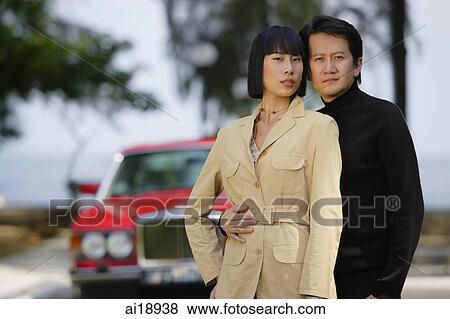 Couple standing side by side, looking at camera, car in the background View Large Photo Image Stock Photo - Couple standing side by side, looking at camera, car in the background. Fotosearch
