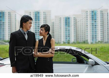 Couple standing side by side next to sports car, looking at each other View Large Photo Image Stock Photo - Couple standing side by side next to sports car, looking at each other. Fotosearch