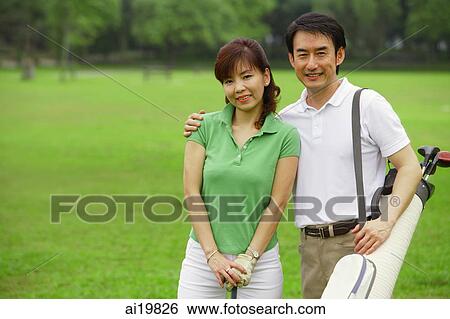 Couple standing side by side on golf course, looking at camera View Large Photo Image Stock Photograph - Couple standing side by side on golf course, looking at camera. Fotosearch