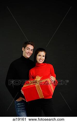 Stock Image - Couple standing side by side, woman holding big gift box. Fotosearch