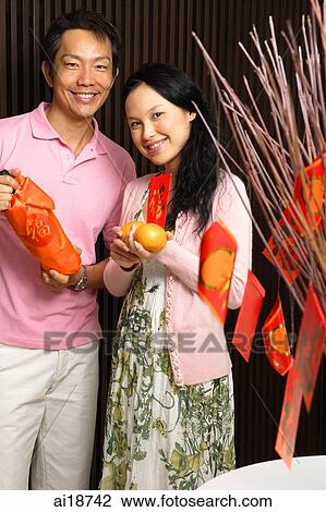 Stock Image - Couple standing together, holding oranges and wine. Fotosearch