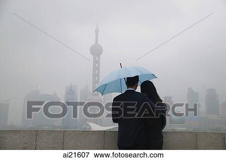 Couple using an umbrella looking at Oriental Pearl TV Tower in the background View Large Photo Image Stock Photo - Couple using an umbrella looking at Oriental Pearl TV Tower in the background. Fotosearch