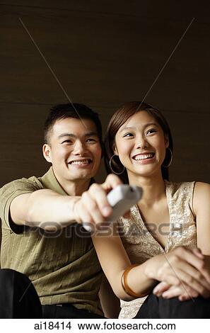 Couple watching TV, man holding remote control View Large Photo Image Picture - Couple watching TV, man holding remote control. Fotosearch
