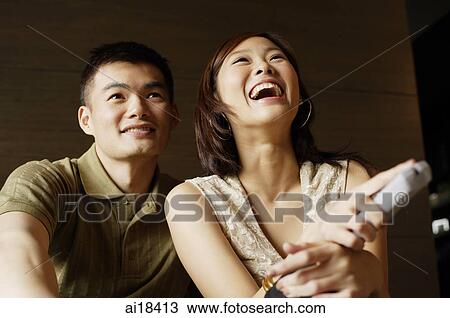 Stock Image - Couple watching TV, woman holding remote control. Fotosearch