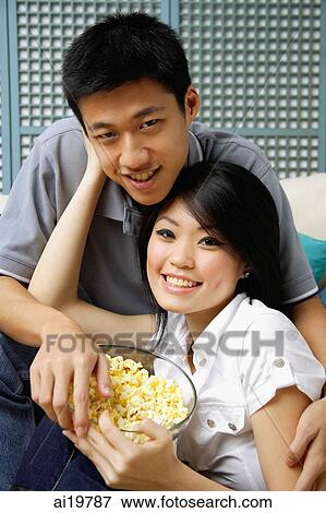 Couple with bowl of popcorn, looking at camera View Large Photo Image Stock Photo - Couple with bowl of popcorn, looking at camera. Fotosearch