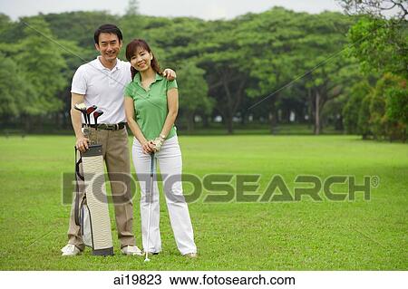 Stock Image - Couple with golf club and golf bag on golf course, smiling at camera. Fotosearch