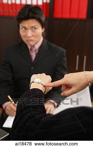 Cropped image showing businesswoman's hands pointing to wrist watch, man in the background, frowning View Large Photo Image Stock Photo - Cropped image showing businesswoman's hands pointing to wrist watch, man in the background, frowning. Fotosearch