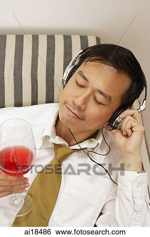 Executive listening to headphones, holding wine glass, eyes closed View Large Photo Image Stock Photograph - Executive listening to headphones, holding wine glass, eyes closed. Fotosearch