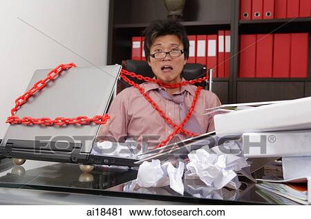 Executive sitting at messy desk, tied to chair and laptop by red chain View Large Photo Image Stock Image - Executive sitting at messy desk, tied to chair and laptop by red chain. Fotosearch