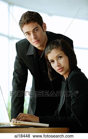 Executives dressed in black, sitting next to laptop, looking at camera, serious expressions View Large Photo Image Stock Photo - Executives dressed in black, sitting next to laptop, looking at camera, serious expressions. Fotosearch