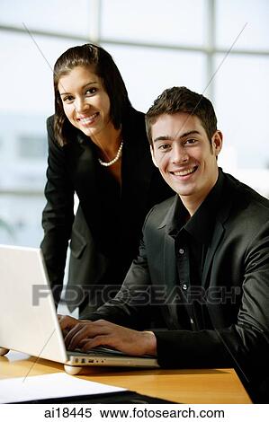 Stock Photography - Executives dressed in black, sitting next to laptop, looking at camera, smiling. Fotosearch