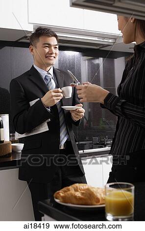 Executives in kitchen, man having coffee, woman holding mobile phone View Large Photo Image Stock Photo - Executives in kitchen, man having coffee, woman holding mobile phone. Fotosearch