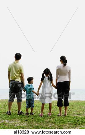 Stock Photo - Family of four, looking out to sea, rear view. Fotosearch