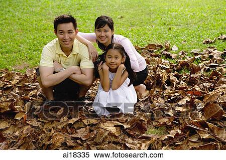 Stock Photography - Family with one child crouching on pile of leaves, looking at camera. Fotosearch