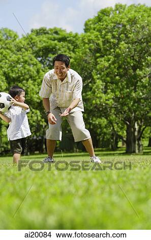 Picture - Father and young son playing with soccer ball in park. Fotosearch