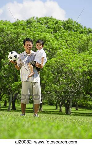 Stock Image - Father carrying young son, both smiling at camera. Fotosearch