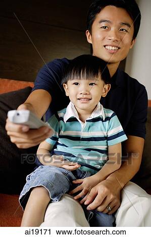 Father with young son on lap, holding TV remote control View Large Photo Image Stock Image - Father with young son on lap, holding TV remote control. Fotosearch