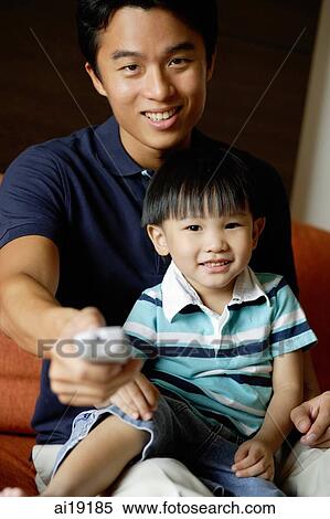 Father with young son on lap, holding TV remote control towards camera View Large Photo Image Stock Photography - Father with young son on lap, holding TV remote control towards camera. Fotosearch