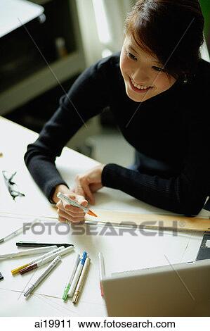 Stock Image - Female designer sitting at table with ruler and felt tip marker. Fotosearch