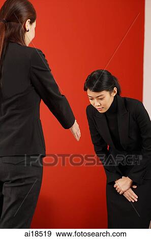 Stock Photo - Female executive bowing to another female executive whose hand is outstretched. Fotosearch