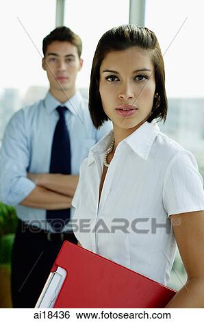 Female executive carrying clipboard, looking at camera, male executive in the background View Large Photo Image Stock Photograph - Female executive carrying clipboard, looking at camera, male executive in the background. Fotosearch