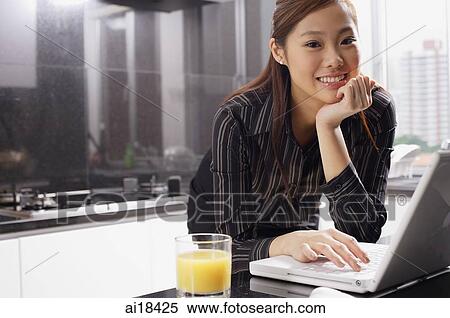 Stock Photography - Female executive in kitchen with laptop, hand on chin, smiling at camera. Fotosearch