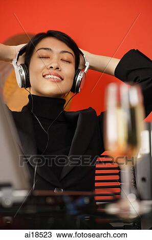 Female executive sitting at desk, listening to headphones, eyes closed, hands behind head View Large Photo Image Stock Image - Female executive sitting at desk, listening to headphones, eyes closed, hands behind head. Fotosearch