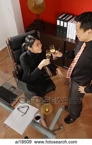 Stock Photo - Female executive sitting in office, toasting drinks with male executive in front of her. Fotosearch