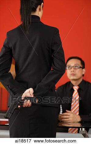 Female executive standing in front of seated male executive, gun behind her back View Large Photo Image Stock Photo - Female executive standing in front of seated male executive, gun behind her back. Fotosearch