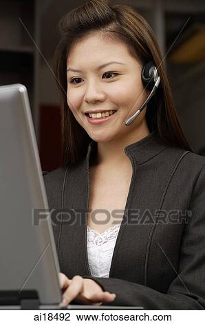Female executive wearing hands free device, looking at laptop View Large Photo Image Stock Image - Female executive wearing hands free device, looking at laptop. Fotosearch