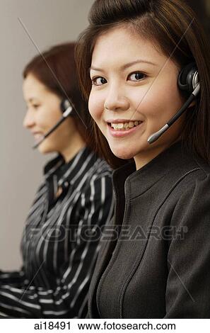 Female executives wearing hands free devices, using laptops, one smiling at camera View Large Photo Image Stock Image - Female executives wearing hands free devices, using laptops, one smiling at camera. Fotosearch