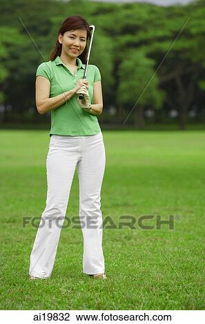 Stock Image - Female golfer with golf club, looking at camera. Fotosearch