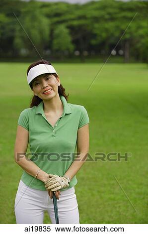 Stock Photography - Female golfer with golf club, smiling at camera. Fotosearch