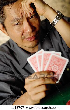 Stock Photo - Gambler holding cards, looking worried. Fotosearch