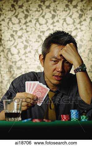 Gambler sitting at table, holding cards, looking worried View Large Photo Image Stock Photograph - Gambler sitting at table, holding cards, looking worried. Fotosearch