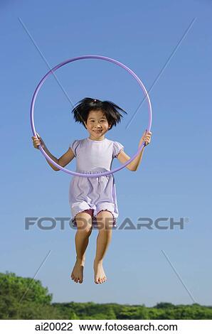 Stock Image - Girl in lavender dress, jumping in mid air, holding hoop. Fotosearch