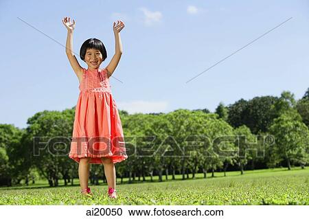 Stock Image - Girl in park, hands in the air, looking at camera. Fotosearch