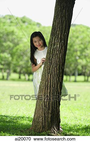 Girl in park, standing behind tree, looking at camera View Large Photo Image Stock Image - Girl in park, standing behind tree, looking at camera. Fotosearch