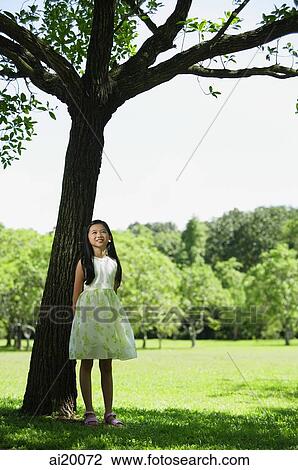 Stock Image - Girl in park, standing under tree. Fotosearch