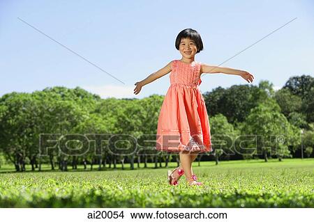 Picture - Girl walking on grass, arms outstretched, smiling. Fotosearch