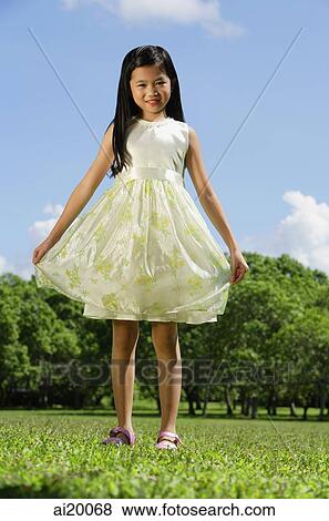 Stock Photo - Girl wearing dress, standing in park, smiling at camera. Fotosearch