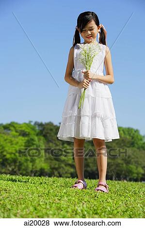 Stock Photo - Girl wearing white dress, holding bouquet of flowers. Fotosearch