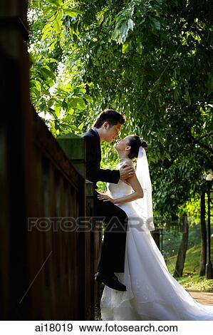 Groom sitting on wall, kissing bride View Large Photo Image Stock Photo - Groom sitting on wall, kissing bride. Fotosearch
