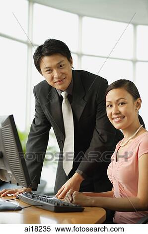 Male executive and female executive by desk in office, smiling at camera View Large Photo Image Stock Photography - Male executive and female executive by desk in office, smiling at camera. Fotosearch