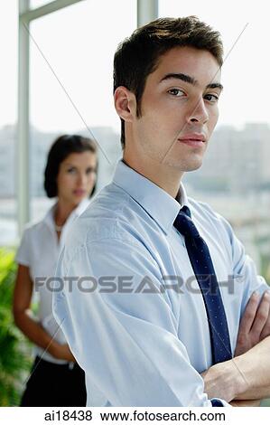 Male executive with arms crossed, looking at camera, woman in the background View Large Photo Image Stock Photo - Male executive with arms crossed, looking at camera, woman in the background. Fotosearch