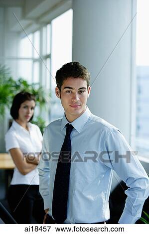 Male executive with hands on hips, looking at camera, woman in the background View Large Photo Image Stock Photo - Male executive with hands on hips, looking at camera, woman in the background. Fotosearch