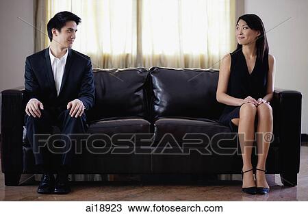 Stock Image - Man and woman sitting apart on sofa, turning to look at each other. Fotosearch
