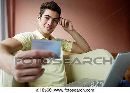 Man at home, using laptop. holding credit card and looking at camera View Large Photo Image Stock Photograph - Man at home, using laptop. holding credit card and looking at camera. Fotosearch