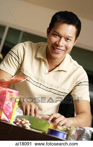 Man at home, wrapping gifts, looking at camera View Large Photo Image Stock Image - Man at home, wrapping gifts, looking at camera. Fotosearch