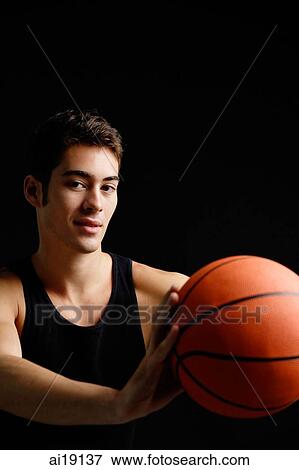 Stock Photo - Man holding basketball, looking at camera. Fotosearch